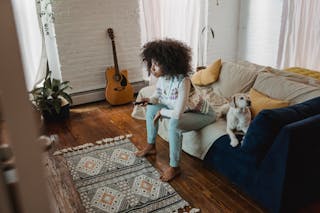 Attentive black woman watching TV near dog at home