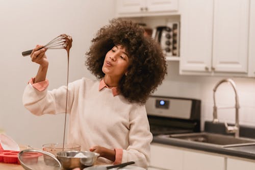 Cheerful black woman with batter flowing from whisk