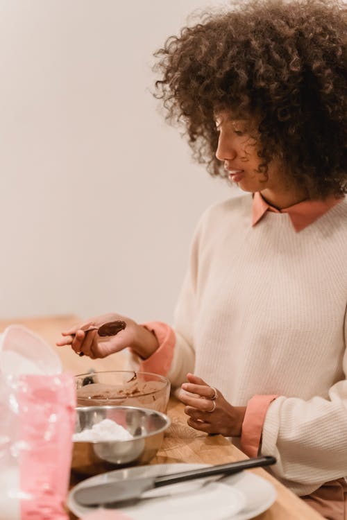 Side view of African American female cook standing at table with bowl of batter and flour while cooking in kitchen