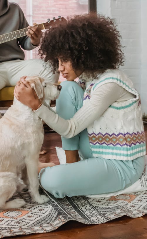 Gentle black woman petting dog near crop guitarist