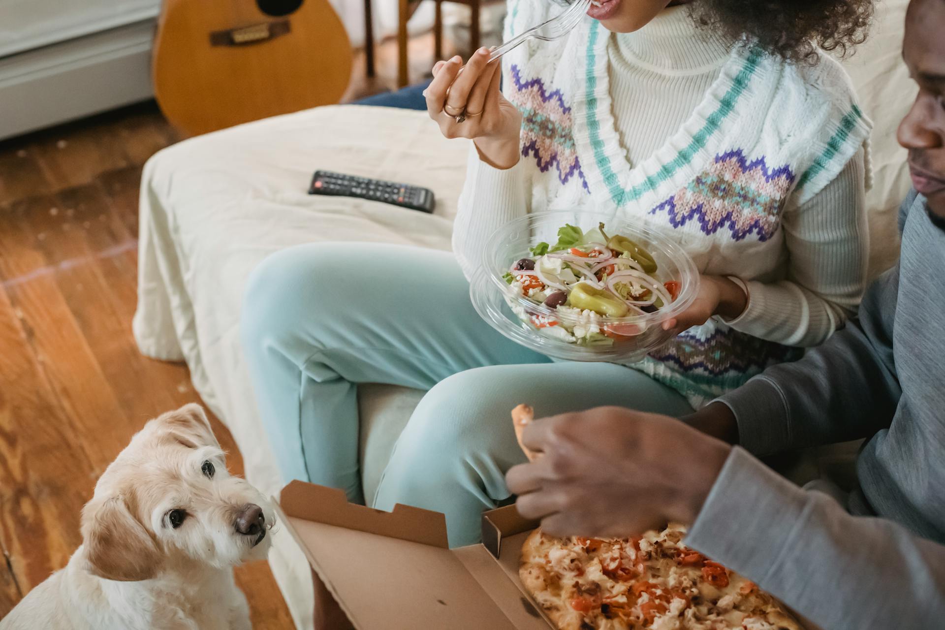 Crop black couple eating food on sofa near dog