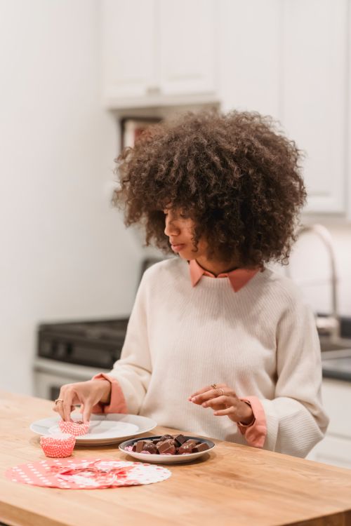 Free Focused African American female serving chocolate candies in molds on plate while standing at table in kitchen with modern equipment Stock Photo
