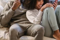 Positive African American couple in casual clothes browsing cellphone on sofa while having fun in cozy living room at home