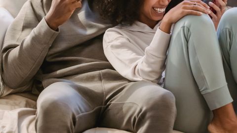 Positive African American couple in casual clothes browsing cellphone on sofa while having fun in cozy living room at home