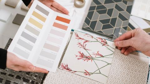 Top view of hands selecting color palettes and textile samples for interior design.