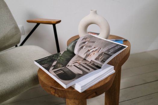 Minimalist interior with an open magazine on a wooden table next to a modern chair.