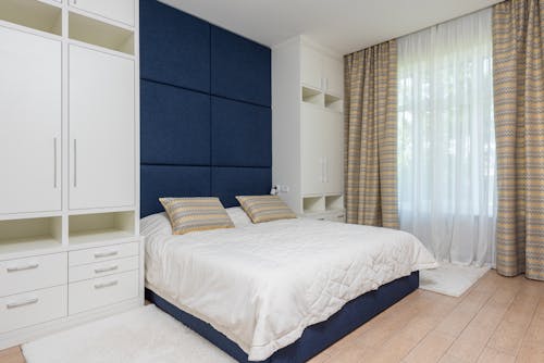 Modern design of comfortable bedroom with wide bed between white wardrobes near big light window and laminate