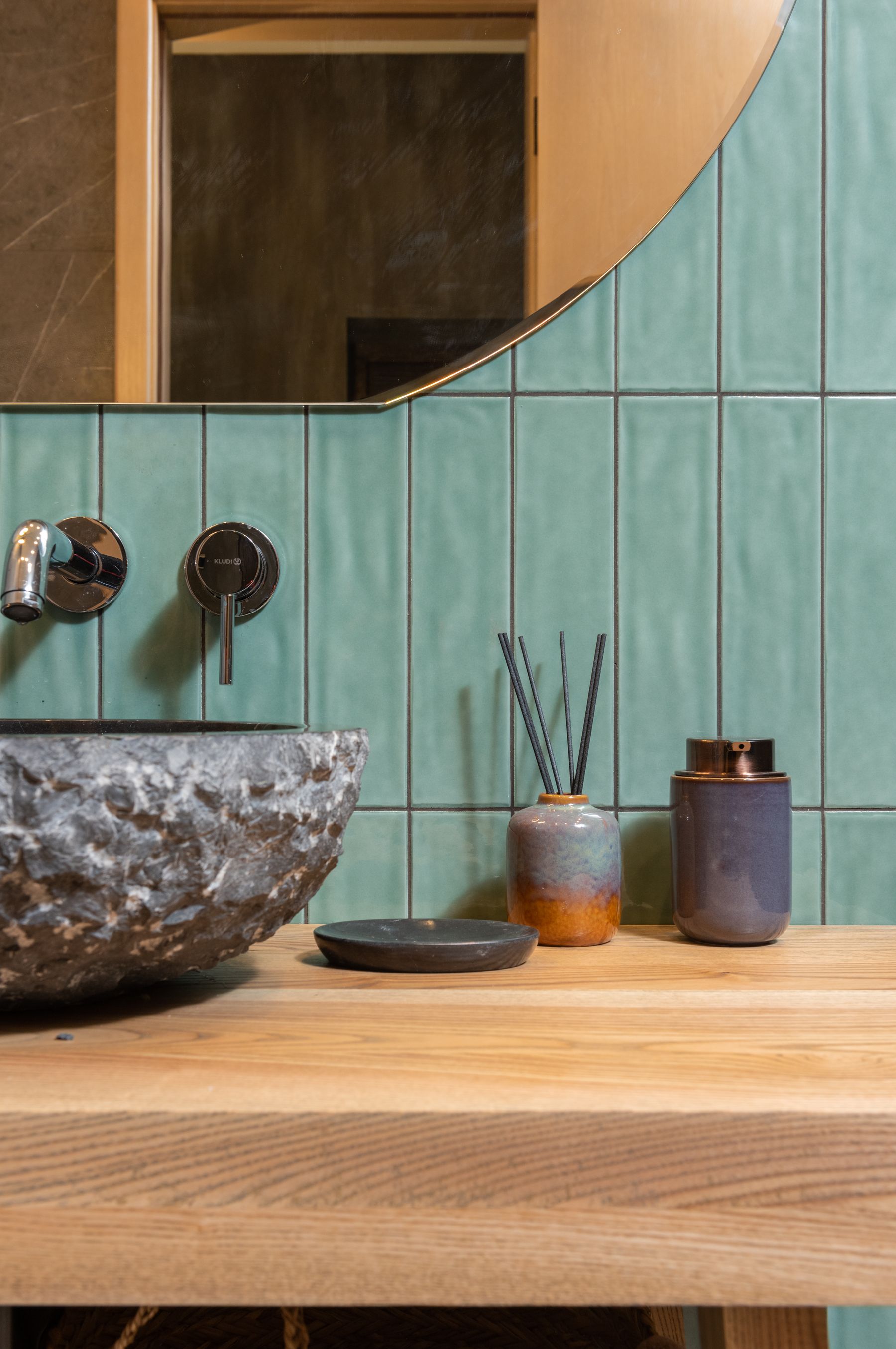 Stone basin, green tile and warm wood combined in an earthy material palette