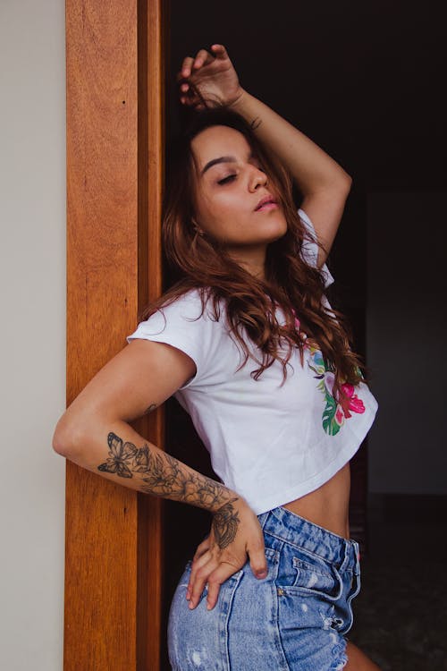 A Tattooed Woman in White Shirt Leaning on the Wall