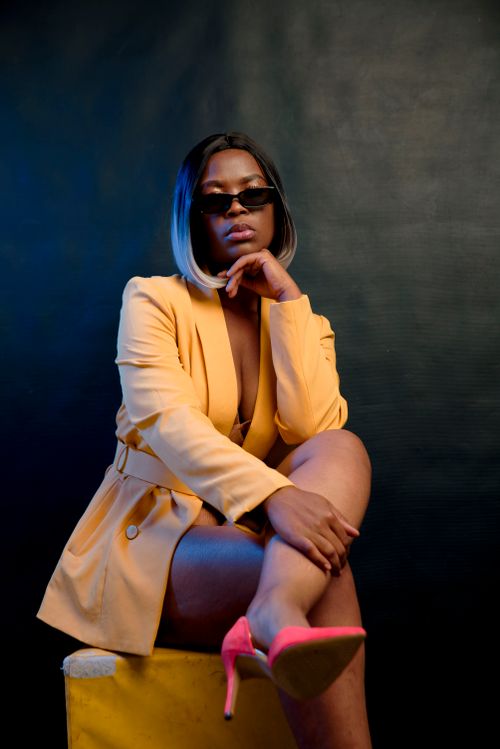 Free Confident woman posing in a yellow coat and sunglasses against a dark background. Stock Photo
