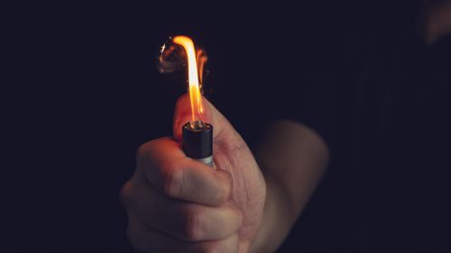 Free Crop anonymous male in black shirt holding bright burning lighter in dark room Stock Photo
