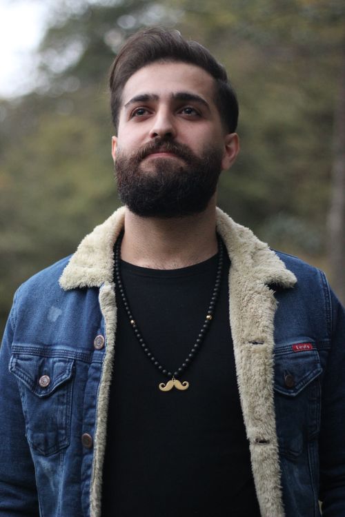 Free Portrait of a bearded man wearing a denim jacket and necklace outdoors. Stock Photo