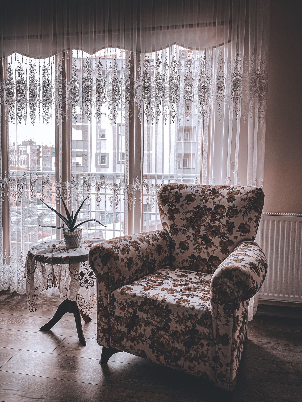 A floral armchair by a window with lace curtains