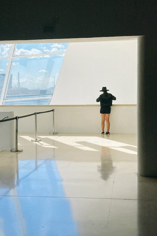 Back view of anonymous female tourist in hat reflecting on tiled floor against window in airport terminal