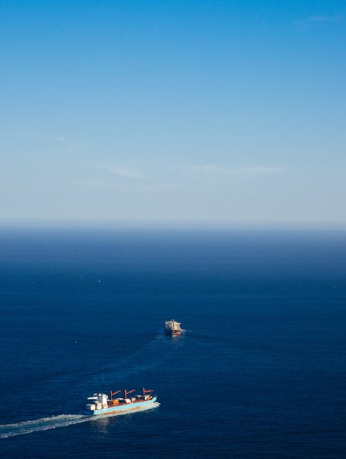 From above of ships sailing on endless ocean under cloudy blue sky during trip in daytime