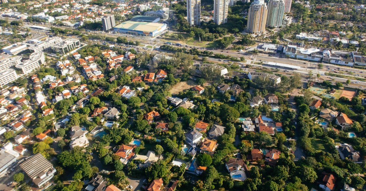 Aerial view of dwelling building exteriors and roofs between lush green trees in summer city