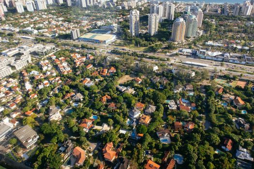 Aerial view of dwelling building exteriors and roofs between lush green trees in summer city
