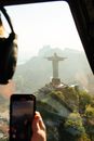 Aerial view of crop unrecognizable pilot in headphones with cellphone in transport against sculpture of Christ Redeemer on mountain in Brazil