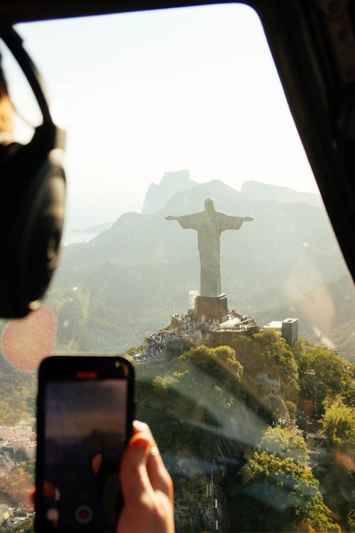 Free Aerial view of crop unrecognizable pilot in headphones with cellphone in transport against sculpture of Christ Redeemer on mountain in Brazil Stock Photo
