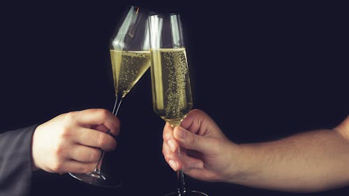 Crop anonymous couple clinking sparkling fine champagne glasses of stylish design against black background