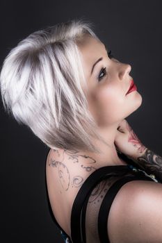 Portrait of a tattooed woman with platinum blonde hair posing in a studio setting, showcasing style and elegance.