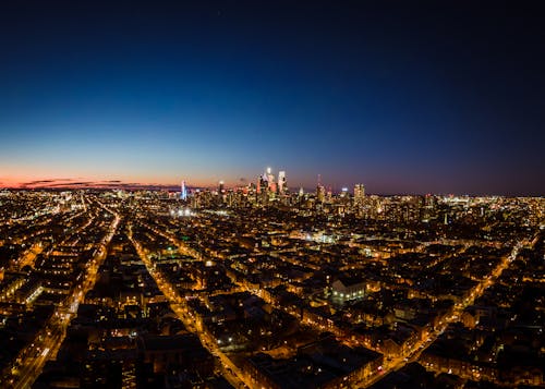 Drone view of contemporary cityscape with illuminated streets under cloudless dark sky at twilight