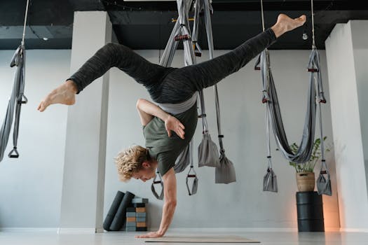 A man performing an aerial yoga pose indoors, showcasing strength and balance.