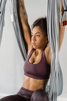 A focused African American woman practicing aerial yoga indoors, emphasizing fitness and wellness.