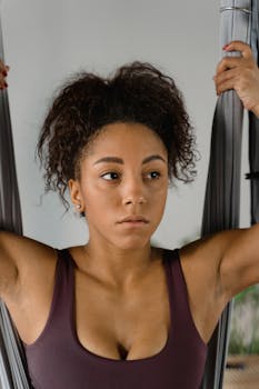 A woman engaging in aerial yoga indoors, concentrating deeply on her pose.