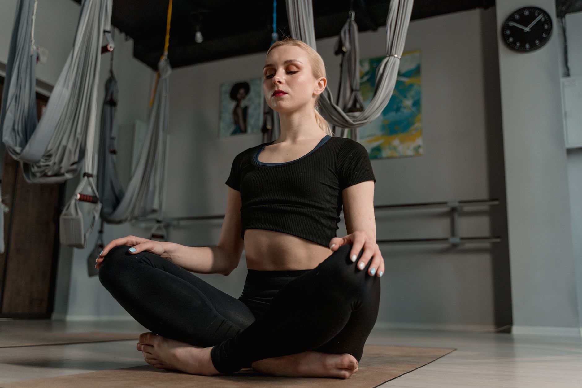 Young woman meditating in a yoga studio with aerial ropes, promoting mindfulness and relaxation.