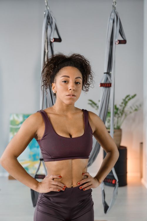 Free A confident woman in activewear stands poised in a fitness studio with aerial yoga hammocks. Stock Photo