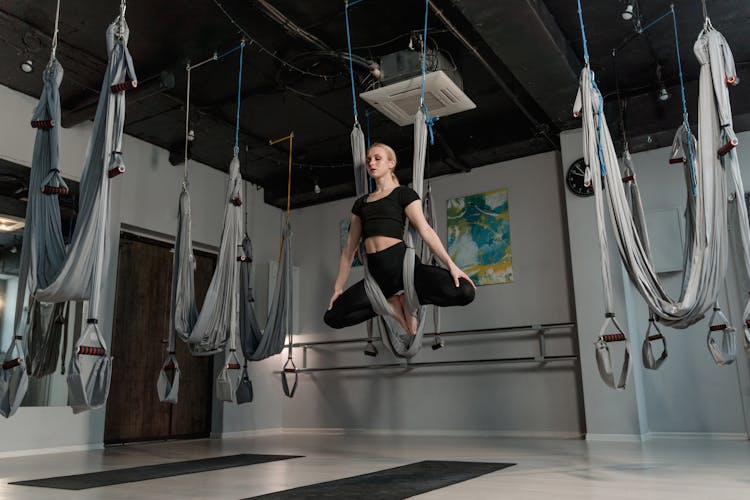 Woman In Black Drop Top And Black Leggings Meditating On An Aerial Yoga Swing