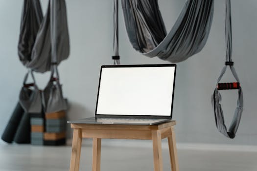 Minimalist yoga studio with aerial hammocks and blank laptop screen on a stool, ideal for diverse wellness themes.
