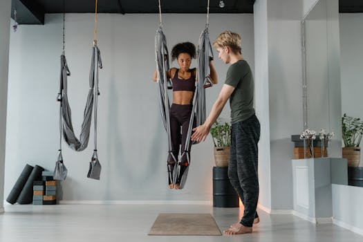 Instructor assists woman practicing aerial yoga in a studio setting with hammocks.