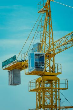 Vertical shot of a large yellow construction crane set against a clear blue sky.
