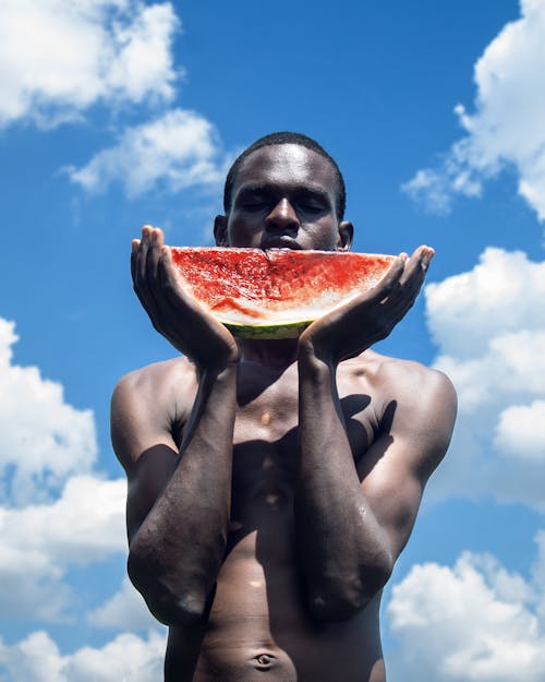 A Shirtless Man Holding a Slice of Watermelon