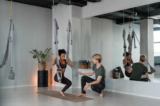 A yoga instructor guides a woman in an aerial yoga class in a minimalist studio.