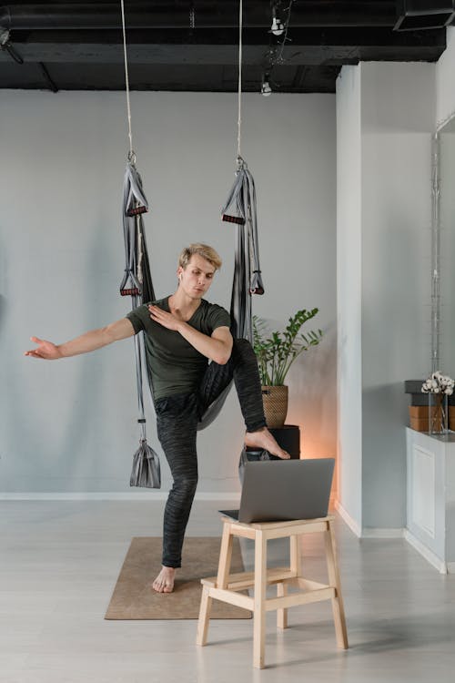 Free Man engaging in aerial yoga exercise indoors with hammock gear Stock Photo