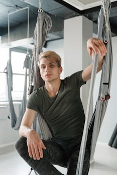 A relaxed young man sits in a hammock at a modern yoga studio, enjoying a moment of calm.