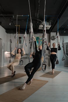 Group of women performing aerial yoga exercises in a well-lit studio setting.