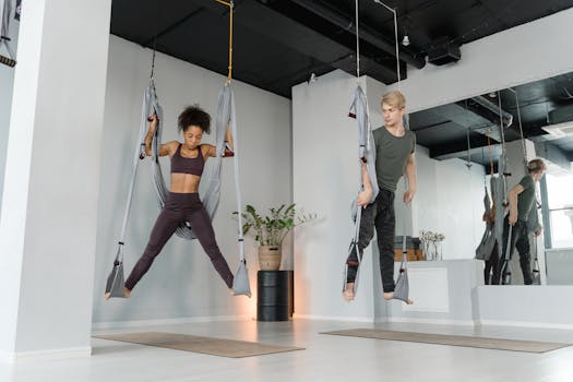 Two people practicing aerial yoga in a bright, modern studio with hammocks.