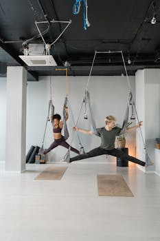 Diverse adults perform aerial yoga in studio using hammocks, promoting wellness.