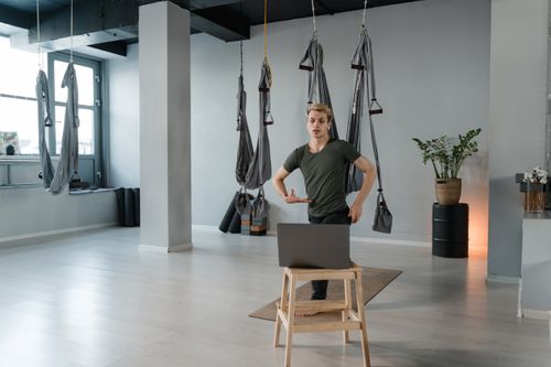 Free A man practicing aerial yoga in a contemporary studio setting using a laptop. Stock Photo