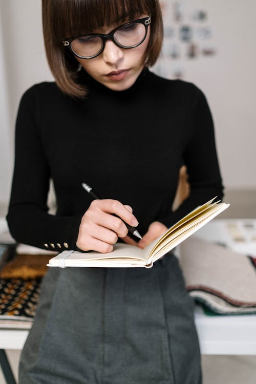A Woman in Black Turtle Neck Writing on Notebook