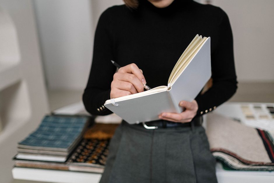 黒い服を着た人がノートに書いており、生地のスウォッチに囲まれている、デザインテーマに最適です。