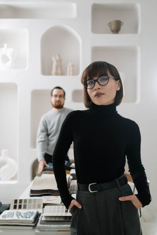 Free Stylish woman in black turtleneck and eyeglasses posing indoors with shelves in background. Stock Photo