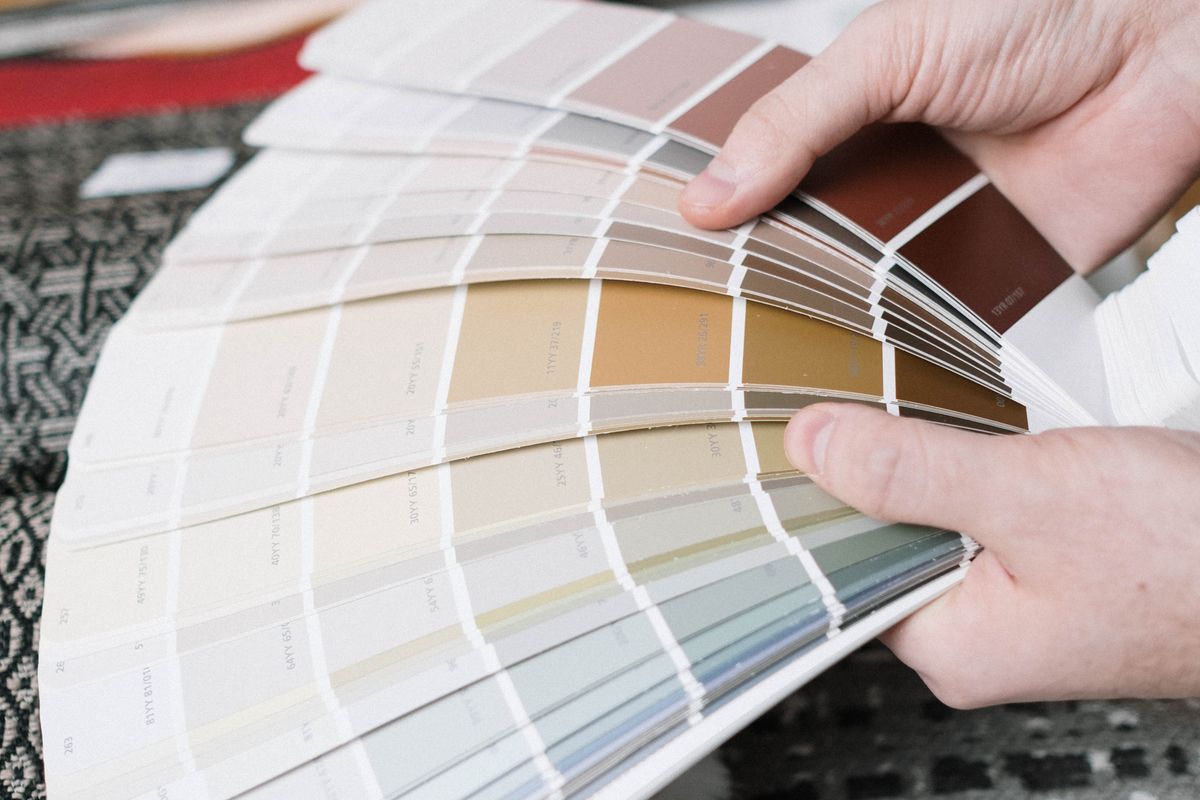 Hands fanning out a deck of paint colour swatches in warm and muted shades