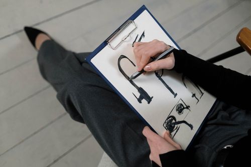 Free A person seated drawing architectural sketches on a white paper with a pencil, captured from above. Stock Photo