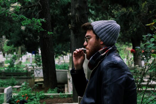 A stylish young man smokes in an urban cemetery setting, showcasing a modern lifestyle.