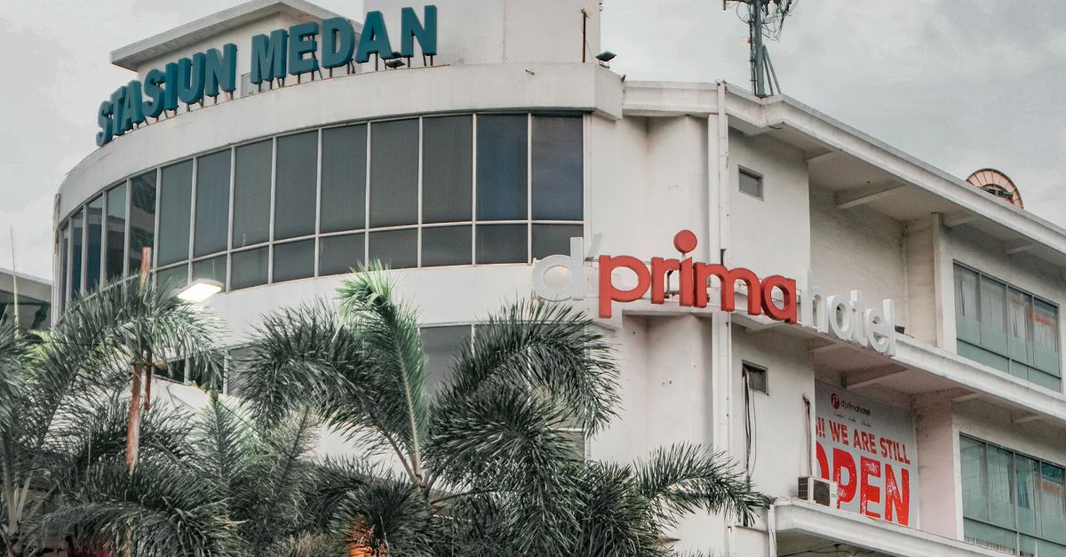 A bustling urban streetscape featuring a prominent building in Medan, Indonesia with palm trees and vehicles.